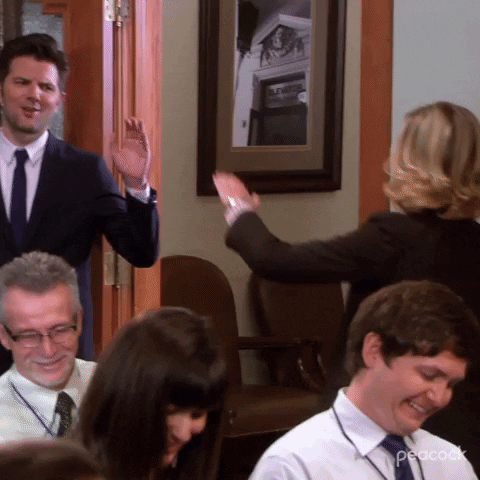 Parks and Recreation gif. Amy Poehler as Leslie walks confidently out of a room and high-fives Adam Scott as Ben