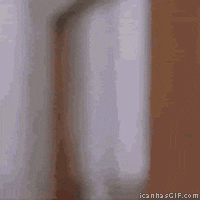 Video gif. Man pops out and back in from a doorway, chewing with a confident expression and giving a thumbs up. 