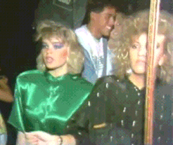 Video gif. Two dancing women with big hair and 80’s clothing do a shimmy.