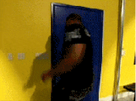 Video gif. A man whips open a blue door and then slaps his foot through it. He punched a hole in it, and then easily rips the top off. He kicks it again.  He’s able to pull the door off the frame and he throws it down to the ground with rage. 