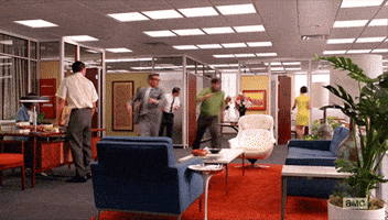 TV gif. From Mad Men, Jay R Ferguson as Stan Rizzo and Harry Hamlin as Jim Cutler race across the office, hopping over sofas and tables in a mad dash.