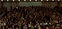Video gif. Inside a ornate performance hall a full house rises in a standing ovation. 