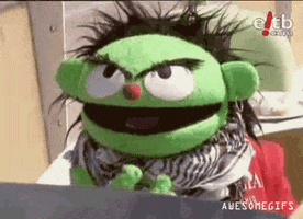 Video gif. Annoyed green puppet slowly lowers his face into his palm in frustration.