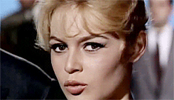 Movie gif. Brigitte Bardot as Brigitte in La Parisienne purses her lips and winks.