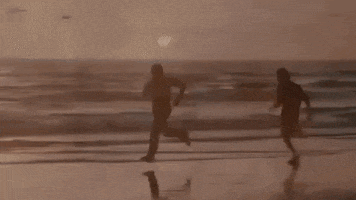 Movie gif. Sylvester Stallone as Rocky and Carl Weathers as Apollo in Rocky. Both of them are booking it down a beach, running as fast as they can. Apollo turns around to run backwards, outpacing Rocky even while backwards. 