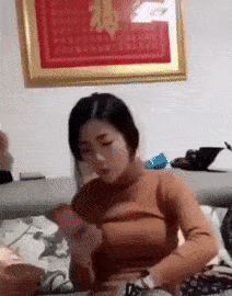 Video gif. Someone comes over to a woman and brushes her hair out of her face and then pulls her turtleneck up over her head and ties a knot, as a prank