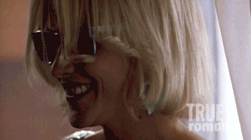 Movie gif. Closeup of Patricia Arquette as Alabama in True Romance wearing silver wayfarers as she takes a drag from a cigarette, then turns toward us and smiles.