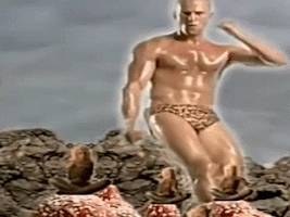 Video gif. Appearing giant in front of a background of a cloudy sky and rocks, an oiled up, muscular man with a glowing aura shows off some interesting dance moves while wearing nothing but leopard print bikini bottoms. He towers over three people sitting crisscrossed and moving meditatively on red rocks.