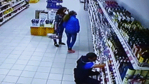 Video gif. Security footage of a liquor store shows two women browsing a wall of wine as a worker takes inventory. As the worker stands up, the shelves full of liquor bottles begin to collapse toward the women, who move quickly out of the way as the bottles crash to the ground at their feet.
