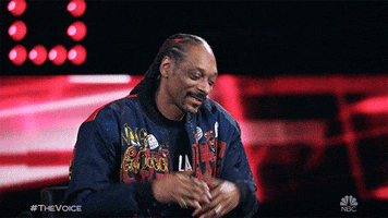 Reality TV gif. Snoop Dogg on The Voice has a warm smile on his face and shrugs, almost presenting himself in a casual way. 
