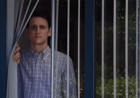 Gif of a sad looking man looking out through some window blinds. 