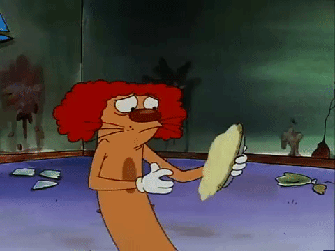 Cat, wearing a clown wig, shoves cream pie in his own face.