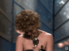 Celebrity gif. Sally Field at the 1985 Academy Awards holds an award in her hands as she raises her bent head with beaming appreciate and raises up both her arms in celebration while mouthing "thank you" to the crowd.