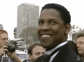 Celebrity gif. Denzel Washington in black tie smiles and waves to the press outside of the 1993 Academy Awards.