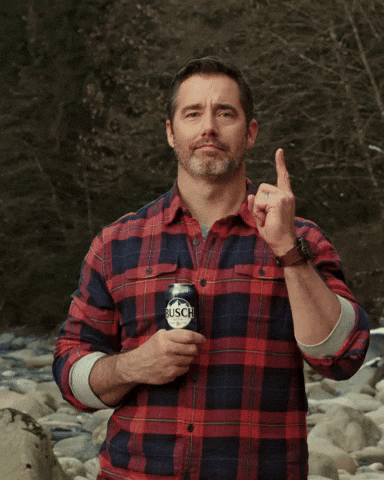 Ad gif. In front of a woodsy creek, a smirking man with a thin beard and a plaid red flannel shirt points upward while holding a can of Busch beer to his chest.