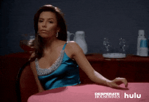 TV gif. Gabrielle Solis from Desperate Housewives leans impatiently in a chair as she strums her fingers on a table in front of her, waiting.