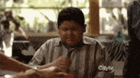 TV gif. Rico Rodriguez as Manny in Modern Family sits at a table during a family meal. Clearly distressed, he squeezes his eyes shut and performs the sign of the cross.