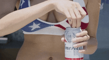 Ad gif. Upper torso of a woman wearing a patriotic bikini top cracks open a can of Budweiser, the beer foam spraying out onto the woman’s hands and chest.