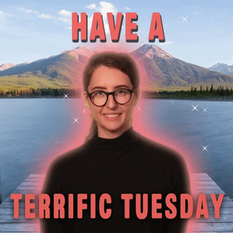 Digital art gif. A serious-looking woman in black, superimposed over a scenic lake and mountain background, says "Have a terrific Tuesday."