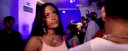 Video gif. A woman at a party makes a dismissive gesture and sticks her tongue out.