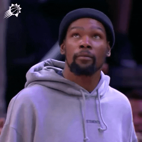 Sports gif. Kevin Durant of the Brooklyn Nets wearing a beanie and sweatshirt looks up and gives a casual salute like he's grateful or relieved about what just happened.