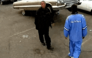 Music video gif. Snoop Dogg does a super chill dance, rolling his shoulders as he walks and sings, wearing dark sunglasses, and long dreadlocks, luxury cars parked in the not-too-distant background. 