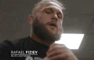 Video gif. Cell phone video zooms in on Rafael Fiziev, a mixed martial artist, flexing his muscles and pumping his extremely strong arms above his head, looking at us with an intimidating expression.