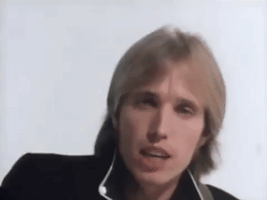 Music video gif. Tom Petty sings as he looks at us, playing a guitar off screen. Text, "Yeah the waiting is the hardest part," with emphasis on the word, hardest. 
