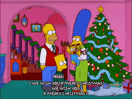 The Simpsons gif. Homer, Marge, Bart, and Maggie wear festive clothing and sway in front of a twinkling Christmas tree as they sing, "We wish you a Merry Christmas."
