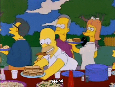 homer simpson is serving food to a group of people at a picnic table .