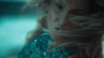 Music video gif. From the video for "Corazon," Claudia Leitte wears a sparkly teal top and bends back, with her hair covering her face, pointing with her finger at us.