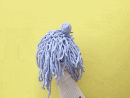 Video gif. A puppet with googly eyes and clacky teeth does a dramatic hair flip.