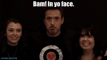 Celebrity gif. Robert Downey Jr. stands in between two smiling women and says confidently, "Bam! In yo face."