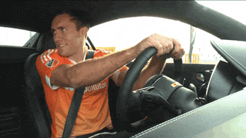 Video gif. Soccer player Andrew Wenger dances in the driver's seat of a car, both hands on the wheel. Safe!