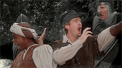 Movie gif. Cary Elwes as Robin Hood and Dave Chappelle as Ahchoo in Robin Hood Men In Tights stand back to back as they hold their arms out to the enemies around them. They both have their mouths open like they’re trying to be intimidating.