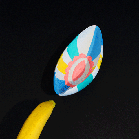 Digital art gif. Banana slides in and out of an oval cup with teal, white, blue, and yellow stripes radiating out from a coral pink scalloped oval at the center.