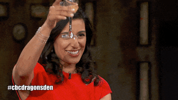 TV gif. People on a stage on Dragon's Den raise their glasses for cheers.
