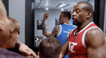 Sports gif. Man tries to hold back a fighter who lunges at another in a crowded doorway.