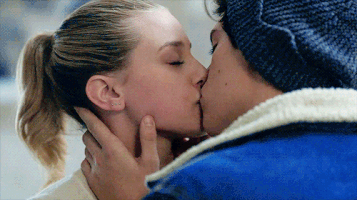 TV gif. Lili Reinhart as Betty and Cole Sprouse as Jughead in Riverdale. They're sharing an intimate kiss and Jughead's hands are gently holding Betty's cheek and neck.