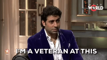 Celebrity gif. Bollywood heartthrob Abhishek Bachchan, dressed in a purple velvet blazer and fine accessories, straightens his collar with self-regard. Text “I'm a veteran at this.”