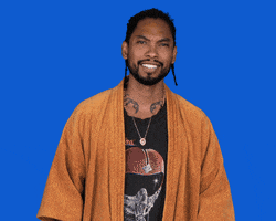 Celebrity gif. Miguel wears a mustard yellow bathrobe, clapping enthusiastically while turning his head side to side, against a bright blue background.