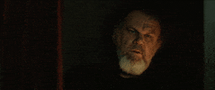 Movie gif. John C. Reilly as Father Tommaso in The Little Hours sits in a confessional furrowing his eyes in confusion and then his eyes shoot open wide from shock.