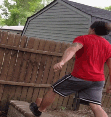 Video gif. Man in a red shirt tries to jump over a wooden fence but fails and falls over the other side, breaking pieces of the fence.