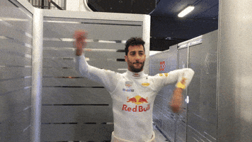 Sport gif. Daniel Ricciardo of Red Bull is stretching out his arms before his Formula One race. He spins his arms in circles at the elbow and he breathes out before smiling and laughing.