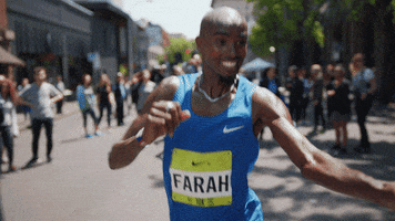 Sports gif. Mo Farah runs in a marathon. He grabs a bottled water from someone and takes a sip out of it. He then pours the rest of the water on his head and tosses it behind him, continuing to run down the street.