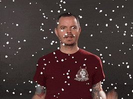 Video gif. A man looks around gleefully before smiling at us as digital snow falls around him. 