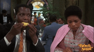 Movie gif. Sidney Poitier, as [TK] in [TK], holds a knife and fork in each hand as he chomps on a corn cob, and his female dining companion glances at him with a worried look as she cuts her food.
