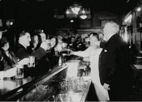 Video gif. Vintage shot of a tavern in the United States in the 1930s celebrating the end of prohibition.
