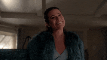 TV gif. Lea Michele as Hester on Scream Queens smiles with her teeth then tightens her lips together and points at someone proudly.