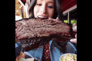 Video gif. Woman holds a big piece of barbecue ribs and chomps into it. She then pulls a piece off and puts it in her mouth.